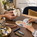 Caregiver holding a blank folded-paper chatterbox while child colours a heart; illustrative art activity, not an exact PDF page